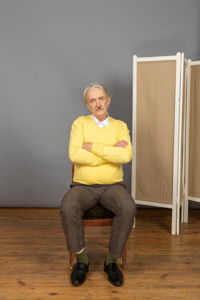 Serious-looking man sitting in chair with crossed arms