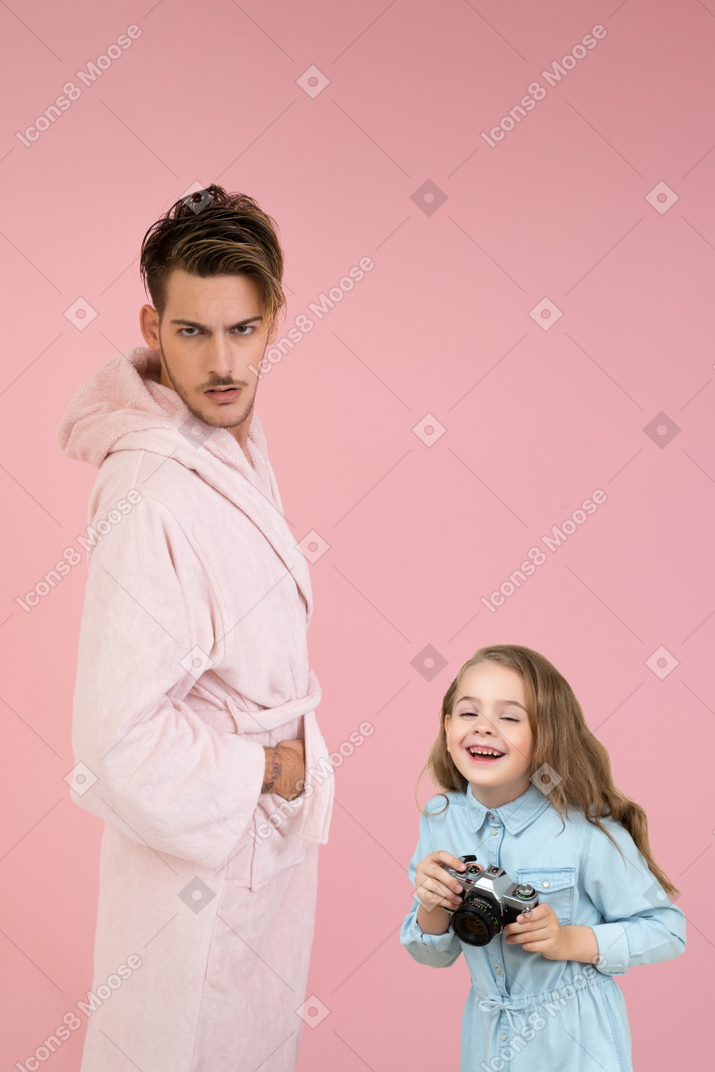 Angry young man and his little daughter holding a camera and laughing