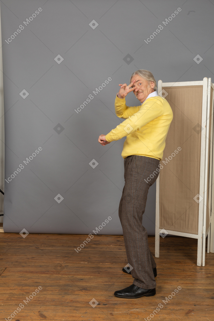 Vista di tre quarti di un uomo anziano che balla cool che mostra un segno di pace