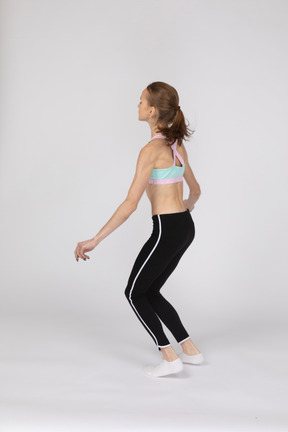 Side view of a teen girl in sportswear squatting and putting hands on hips