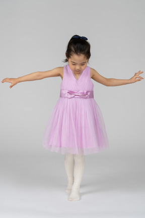 Chica con un vestido rosa manteniendo el equilibrio con los brazos extendidos