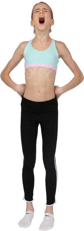 Front view of a teen girl in sportswear yawning and putting hands on hips