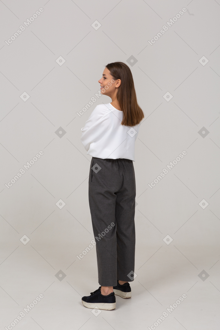 Three-quarter back view of a smiling young lady in office clothing looking aside