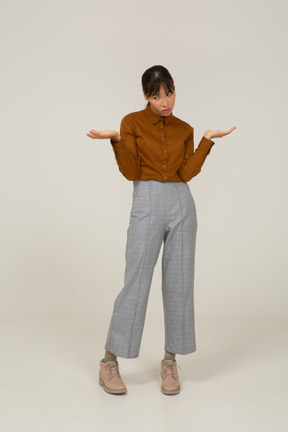 Front view of a questioning young asian female in breeches and blouse raising hands
