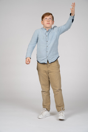 Vista frontal de um menino de pé com o braço levantado e olhando para cima