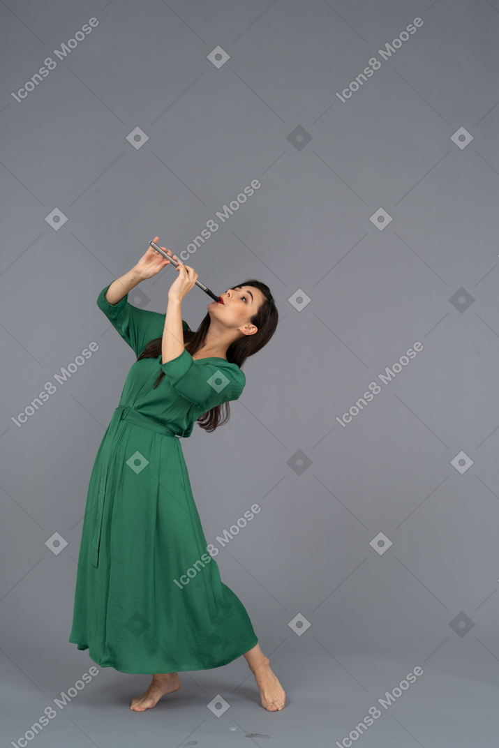 Three-quarter view of a young lady in green dress playing flute while leaning back