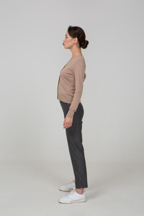 Side view of a young lady standing still in pullover and pants putting hand on hip and pouting