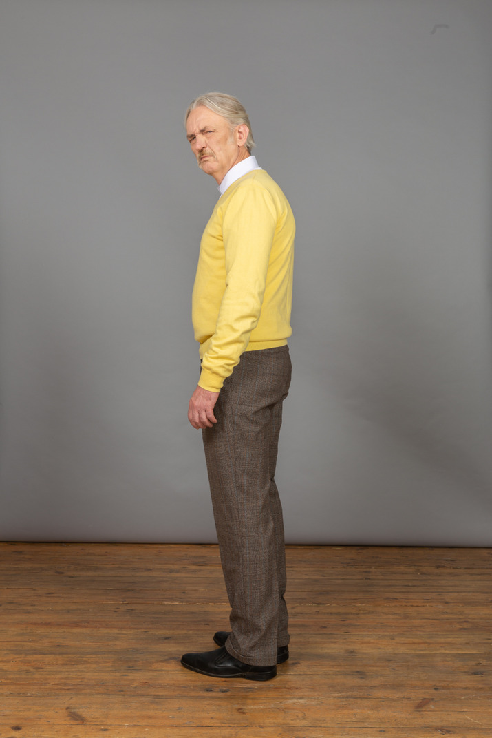Side view of a displeased old man wearing yellow pullover and looking at camera