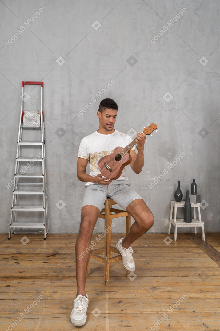 Front view of a man on a stool examining an ukulele