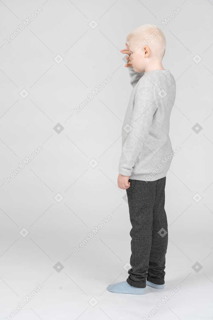 Back three-quarter view of a lonely kid boy in casual clothes touching forehead