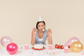 Young asian woman sitting at the birthday table and eating a cake