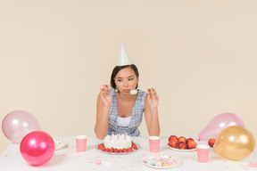 Junge asiatische frau, die am geburtstagstisch sitzt und einen kuchen isst