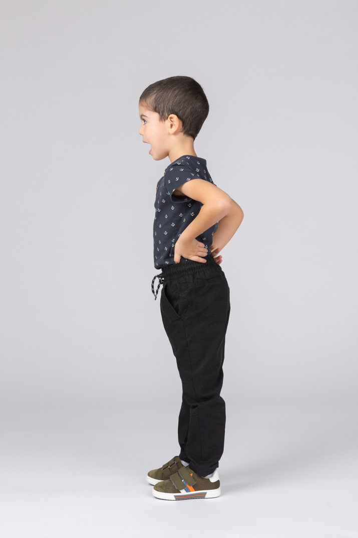 Side view of a cute kid boy standing with hands on hips Photo