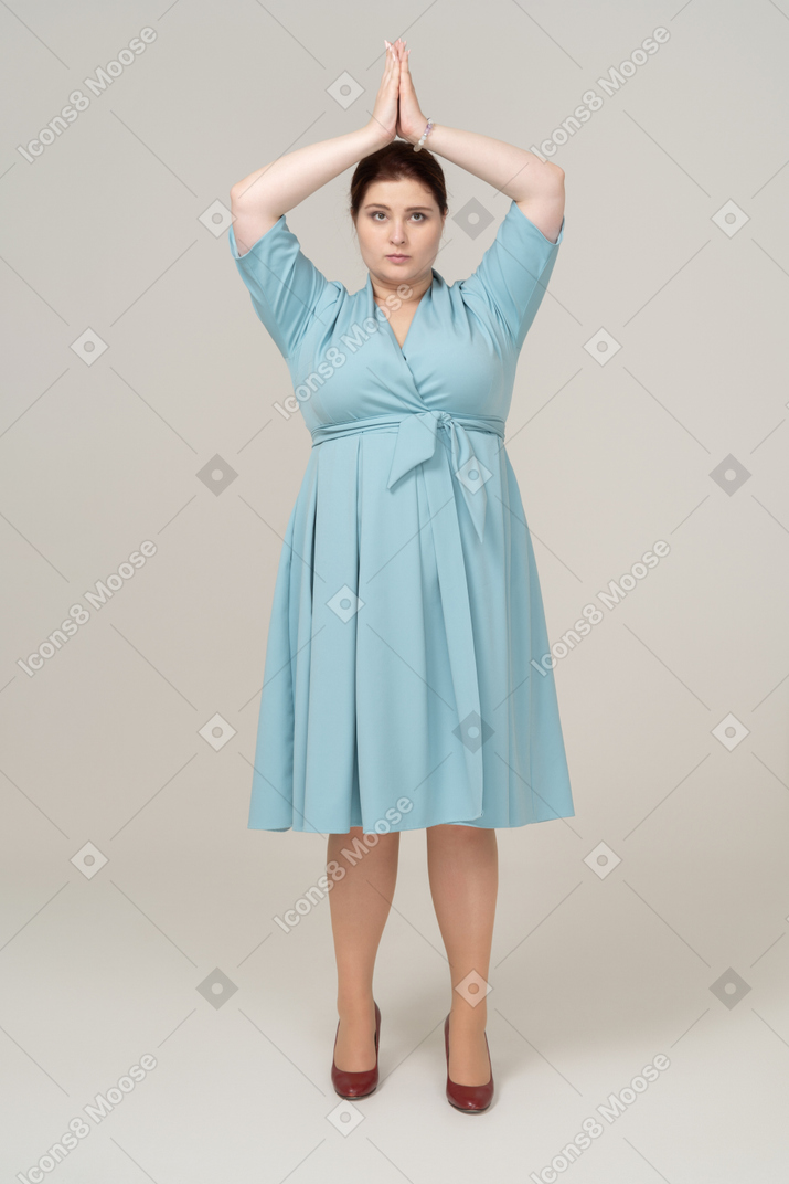 Front view of a woman in blue dress posing with hands over head