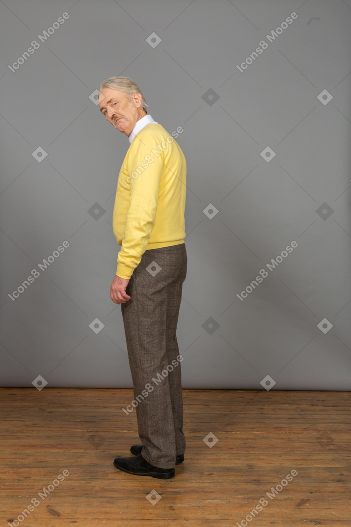 Vista lateral de um velho suspeito com uma camisola amarela a olhar para a câmara