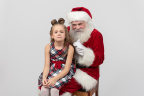 Almost crying kid girl sitting on santa's knees and he's clapping hands