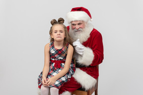 Presque pleurer fille enfant assis sur les genoux du père noël et il applaudit des mains