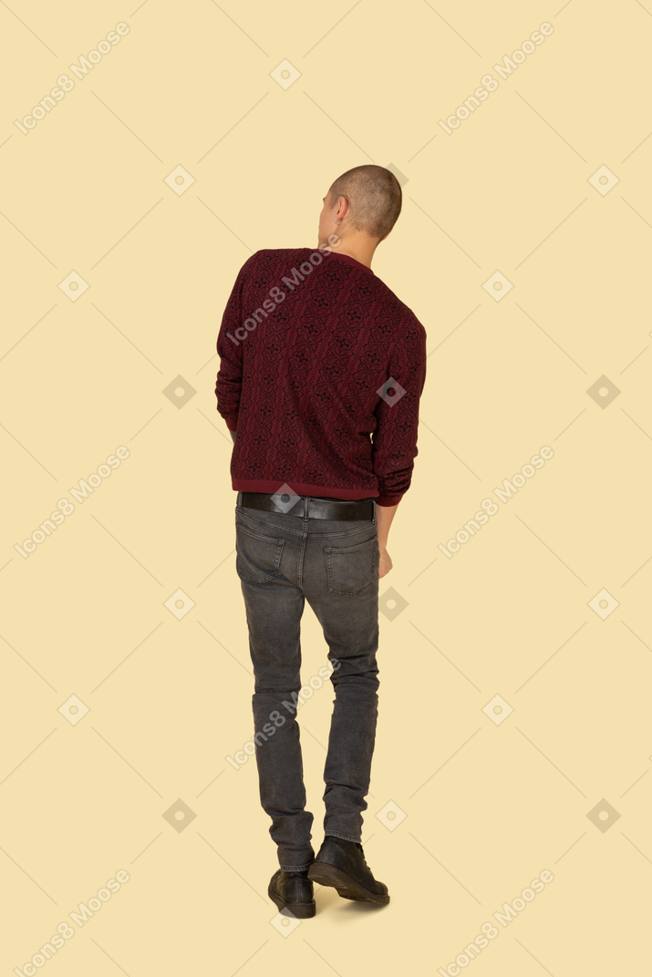 Вид сзади идущего молодого человека в красном пуловере