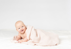 Smiling baby boy covered in beige knitted blanket