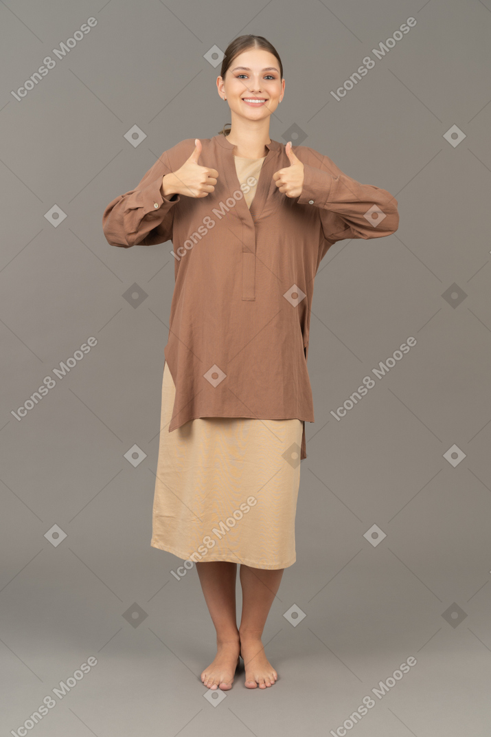Vista frontal da jovem mulher descalça sorrindo e mostrando os polegares