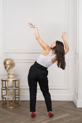 Vista traseira de uma jovem mulher levantando as mãos e inclinando o corpo em pé perto da escultura dourada grega