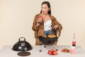 Joven asiática bebiendo coca cola y haciendo barbacoa