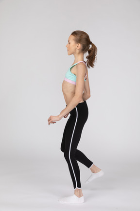 Side view of a teen girl in sportswear tilting shoulders raising leg