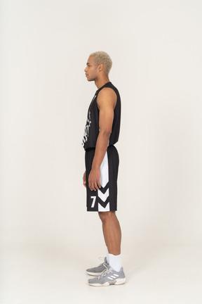 Vista laterale di un giovane giocatore di basket maschile in piedi immobile