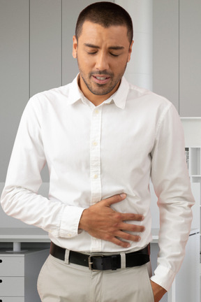 A man in a white shirt is holding his stomach