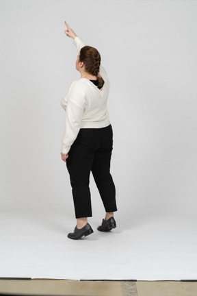 Retrovisor de uma mulher gorducha em roupas casuais em pé com o braço levantado
