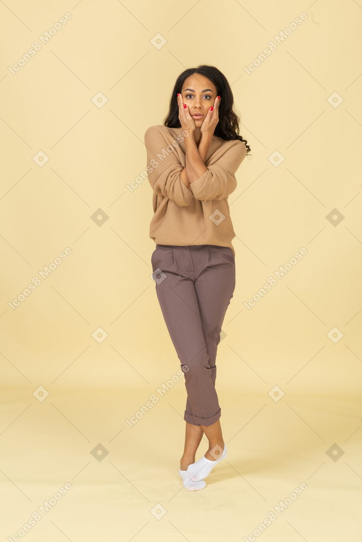 Vista frontal de uma jovem mulher de pele escura tocando as bochechas