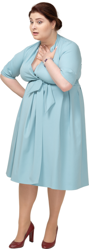 Vista frontal de una mujer sorprendida en vestido azul tocando su cuello