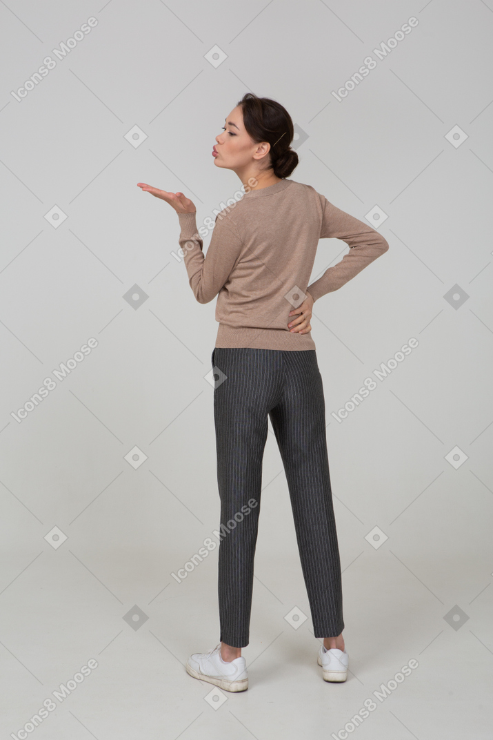 Vista posterior de una joven en suéter y pantalones enviando un beso al aire
