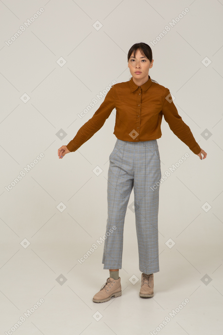 Vista frontal de uma jovem mulher asiática de calça e blusa estendendo os braços