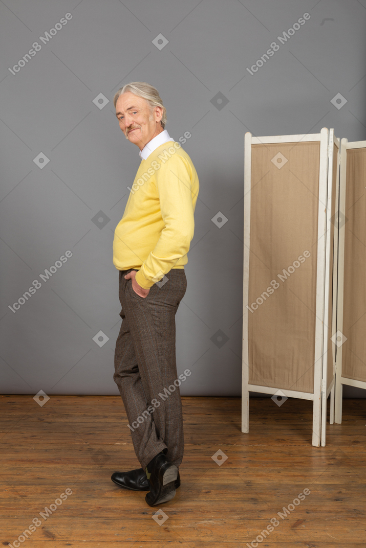 Vista lateral de un anciano sonriente poniendo la mano en el bolsillo mientras mira a la cámara