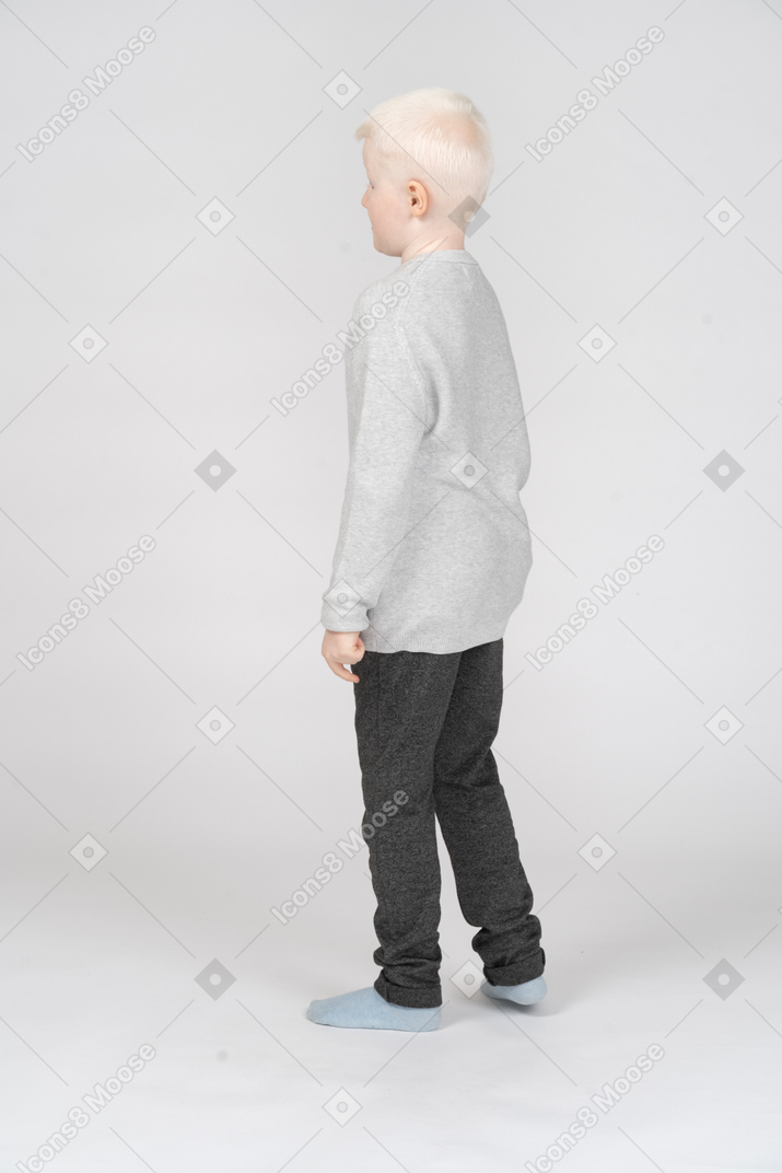 一个小男孩弯曲腿站立的四分之三后视图