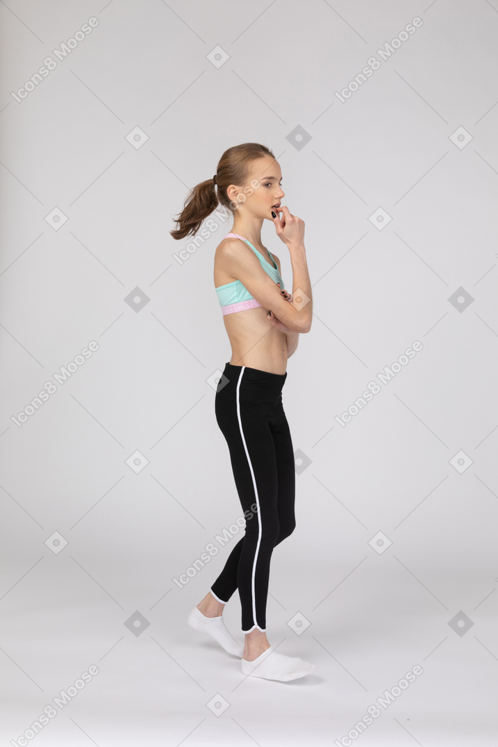 Three-quarter view of a thoughtful teen girl in sportswear biting her finger