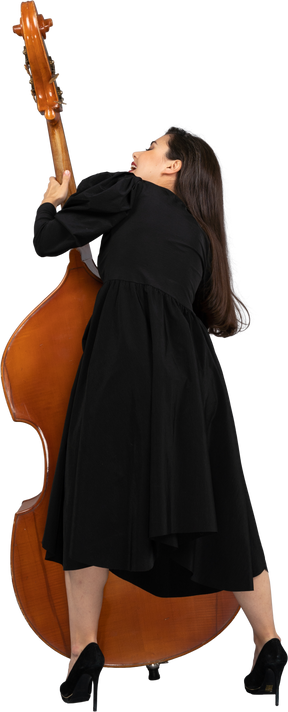 Vista de trás de uma jovem musicista vestida de preto segurando seu contrabaixo