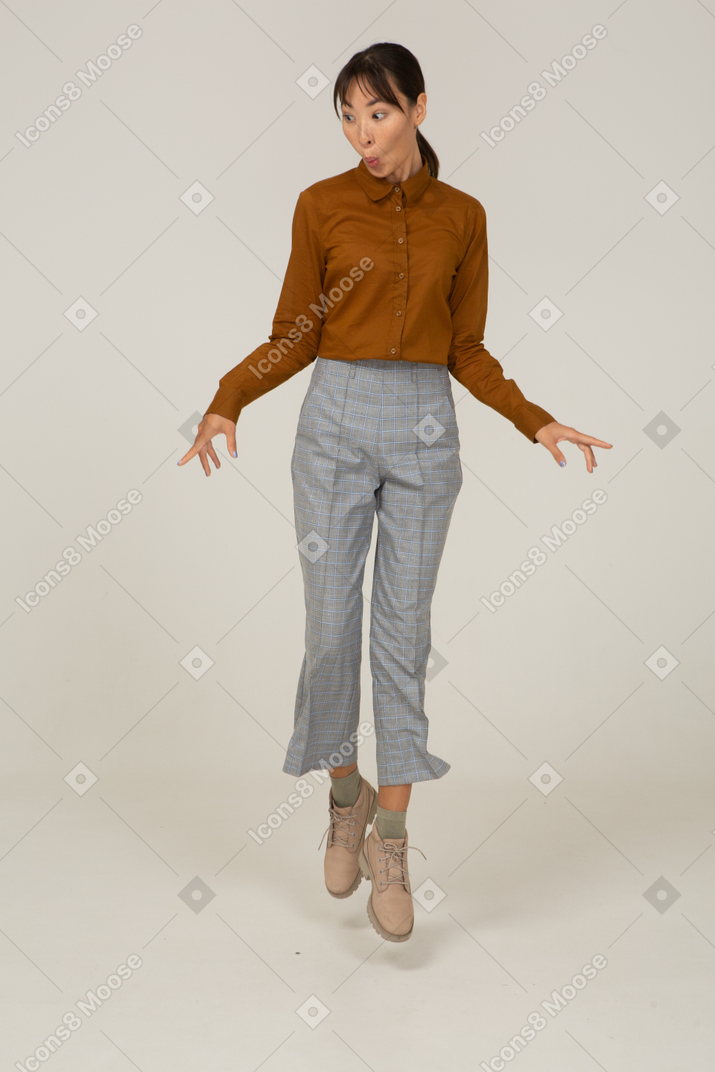 Front view of a jumping young asian female in breeches and blouse outspreading hands