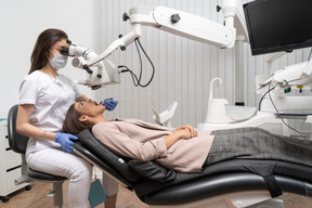 De cuerpo entero de una dentista curando a su paciente y mirando a través del microscopio