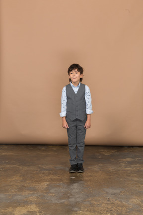 Vista frontal de un niño en traje parado y mirando a la cámara