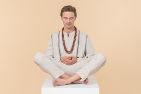 Young caucasian man with necklace sitting in lotus pose with his eyes closed