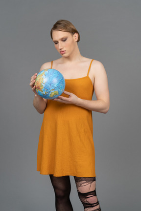 Young non-binary person in orange dress holding globe