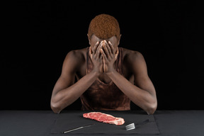 Front view of a withdrawn young afro man sitting near meat