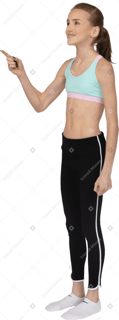 Vista de tres cuartos de una jovencita en ropa deportiva apuntando con el dedo y sonriendo