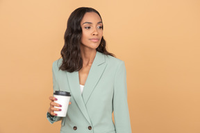 Mujer de negocios elegante sosteniendo una taza de café y mirando a un lado