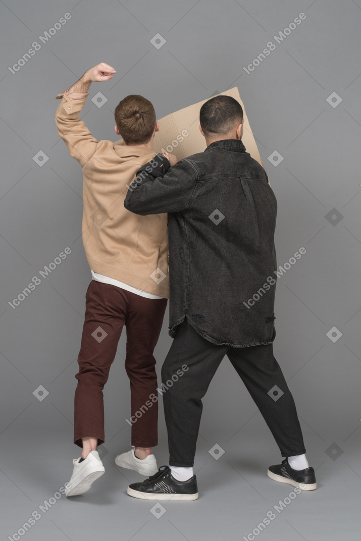 Back view of two agitated young men with a billboard and a raised fist