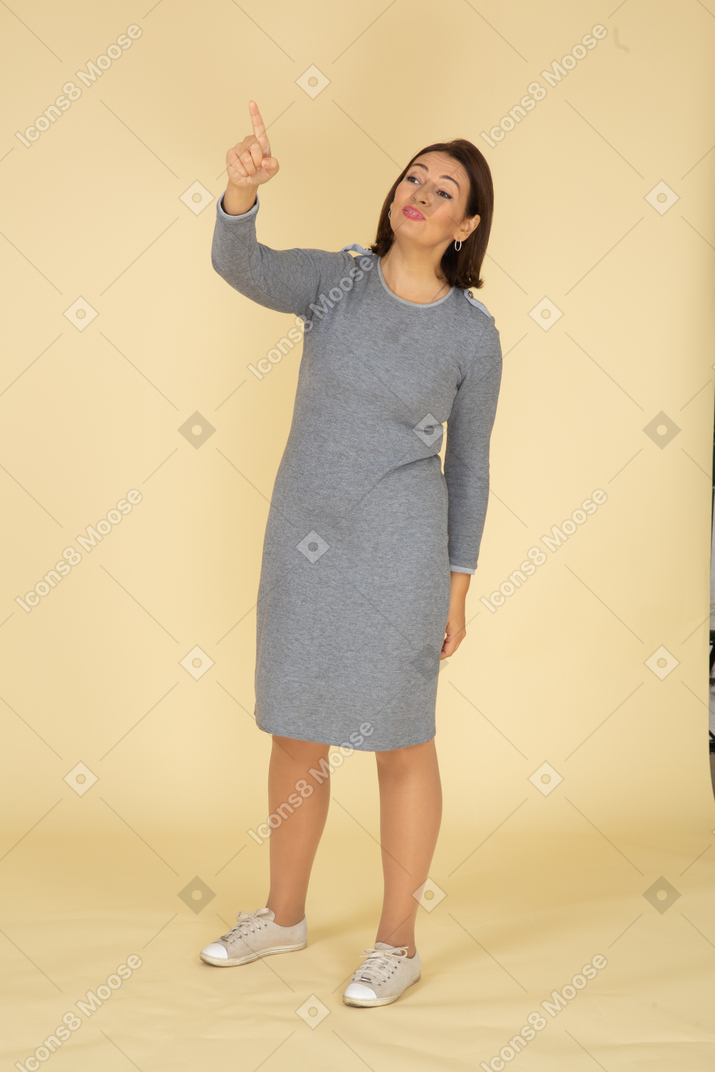 Front view of a woman in grey dress pointing with a finger