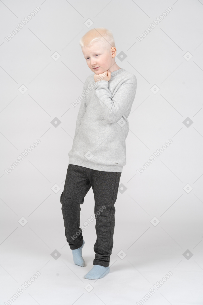 Three-quarter view of a thoughtful kid boy walking and touching chin