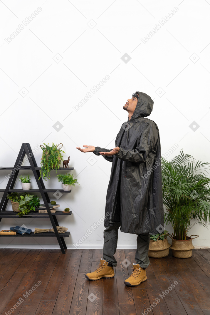 Вид сбоку на мужчину в плаще, ловящего капли дождя